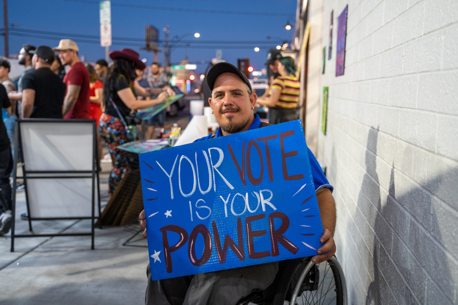 A person sitting in a wheelchair smiling, holding a sign reading ?Your vote is your power?