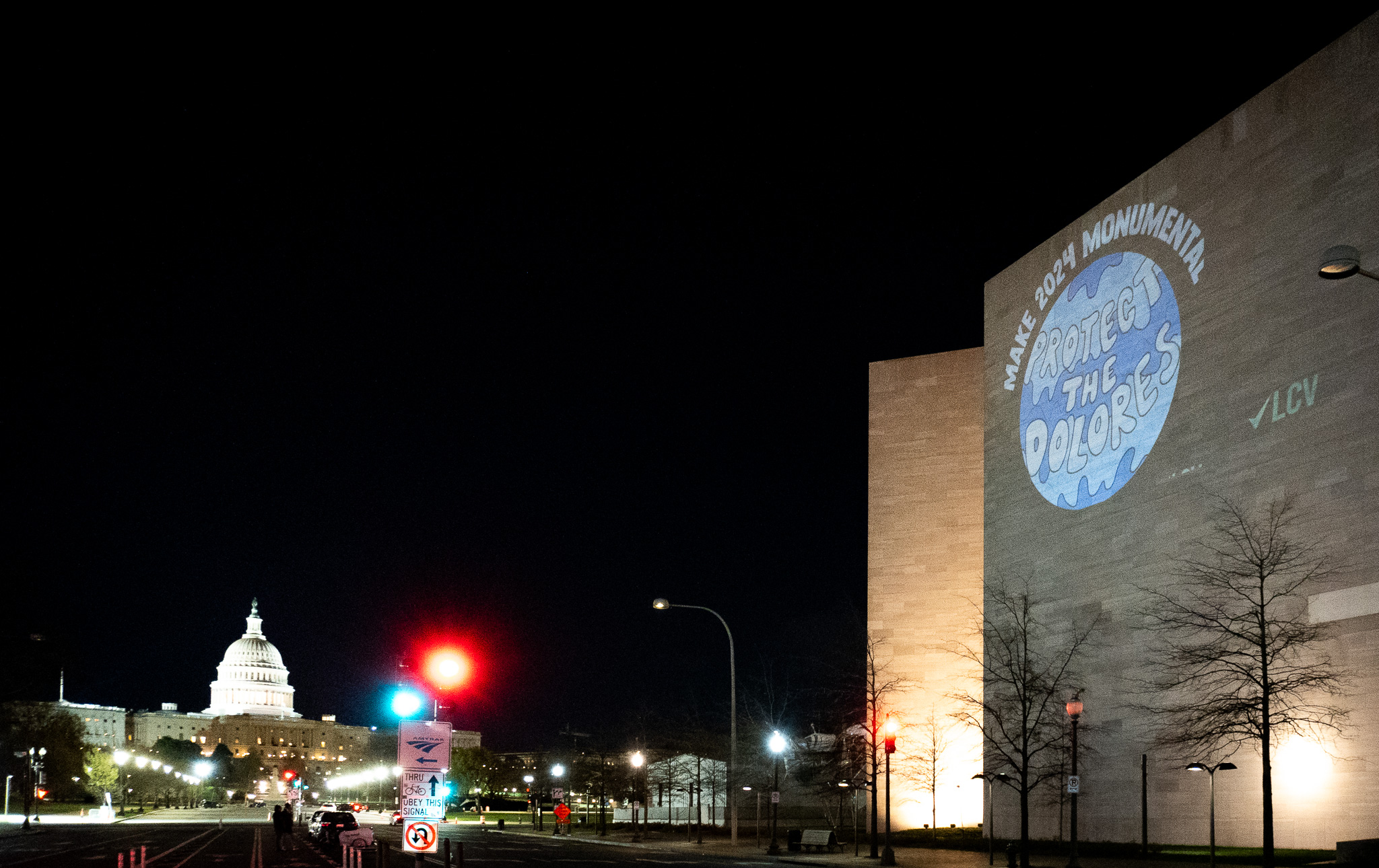 Department of Interior building at night with a light projection on the wall reading "Make 2024 Monumental, Protect the Dolores" and the Capitol in the background.